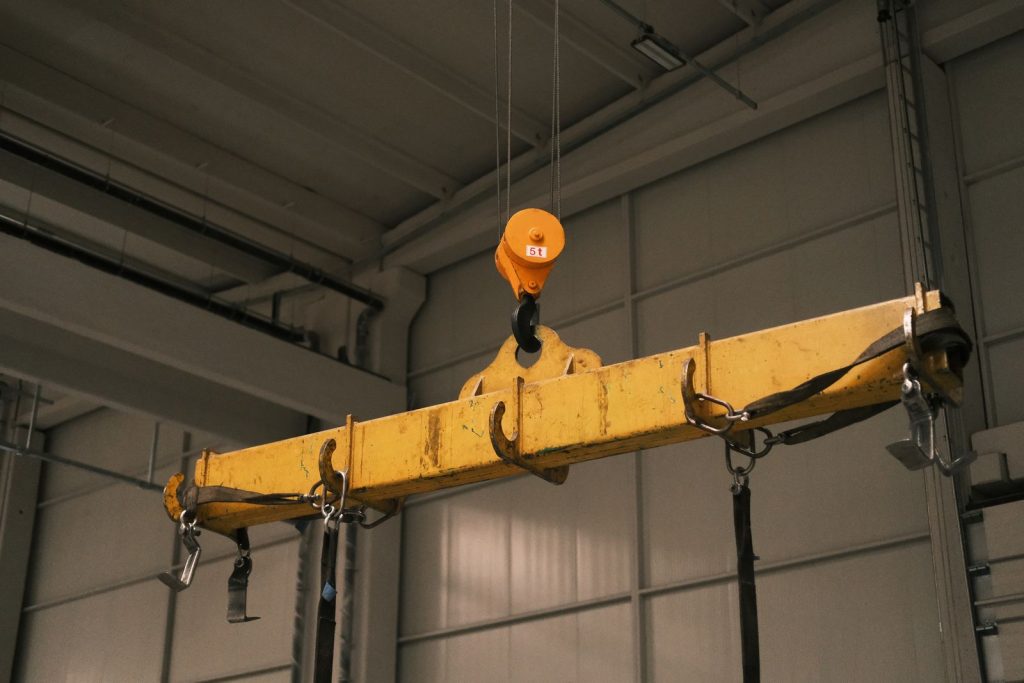 yellow overhead crane hook and lifting beam inside an industrial warehouse