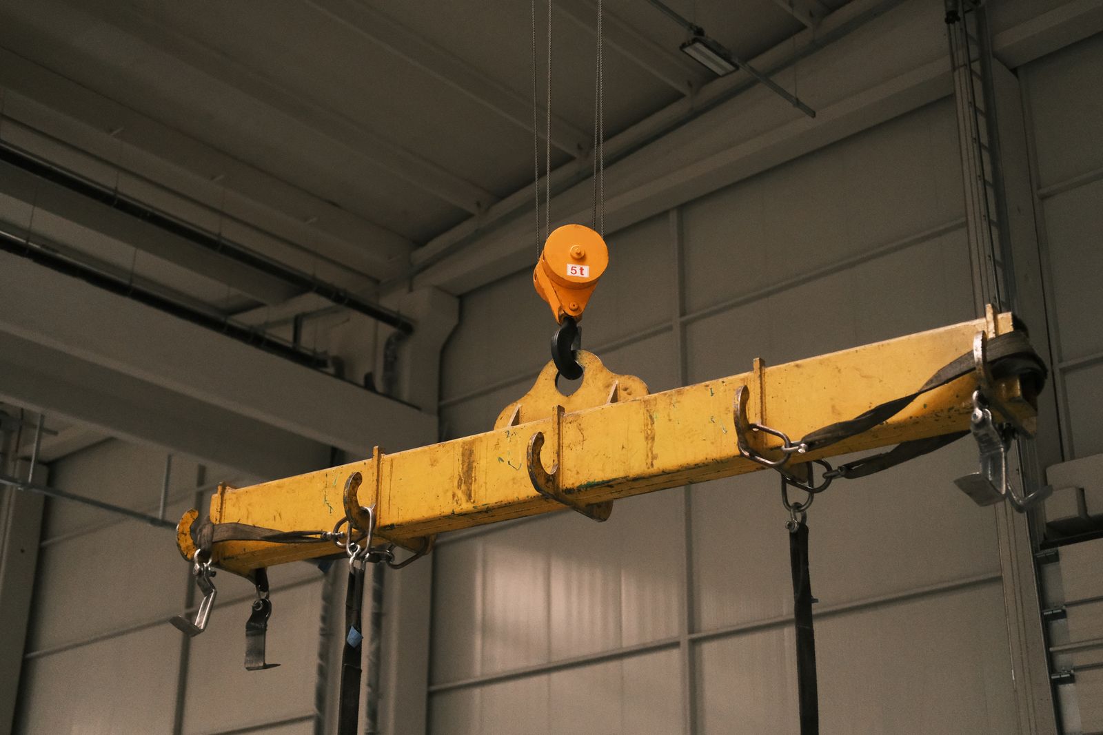 yellow overhead crane hook and lifting beam inside an industrial warehouse