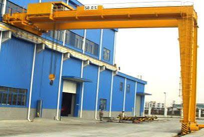 Yellow semi gantry crane operating beside an industrial workshop